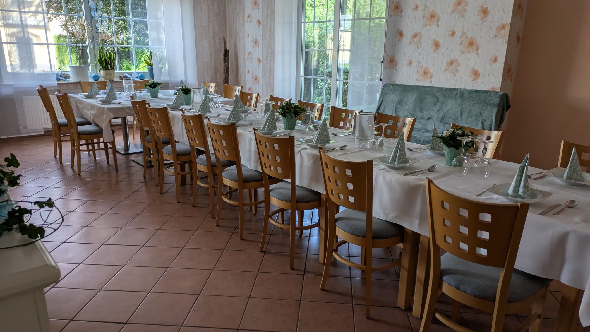 Kleiner Saal – lange Tafel mit Blumenschmuck vor großen Fenstern
